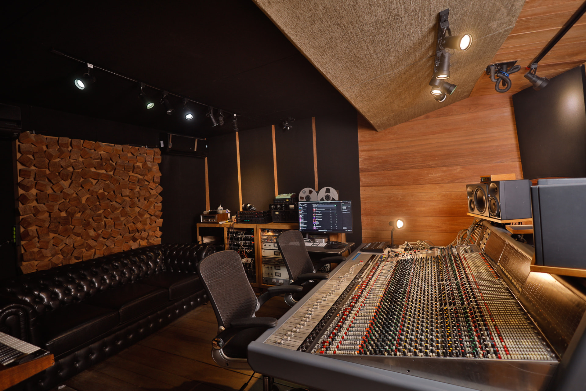 Sala de controle completa do estúdio, com console, sofá de couro e difusores de madeira