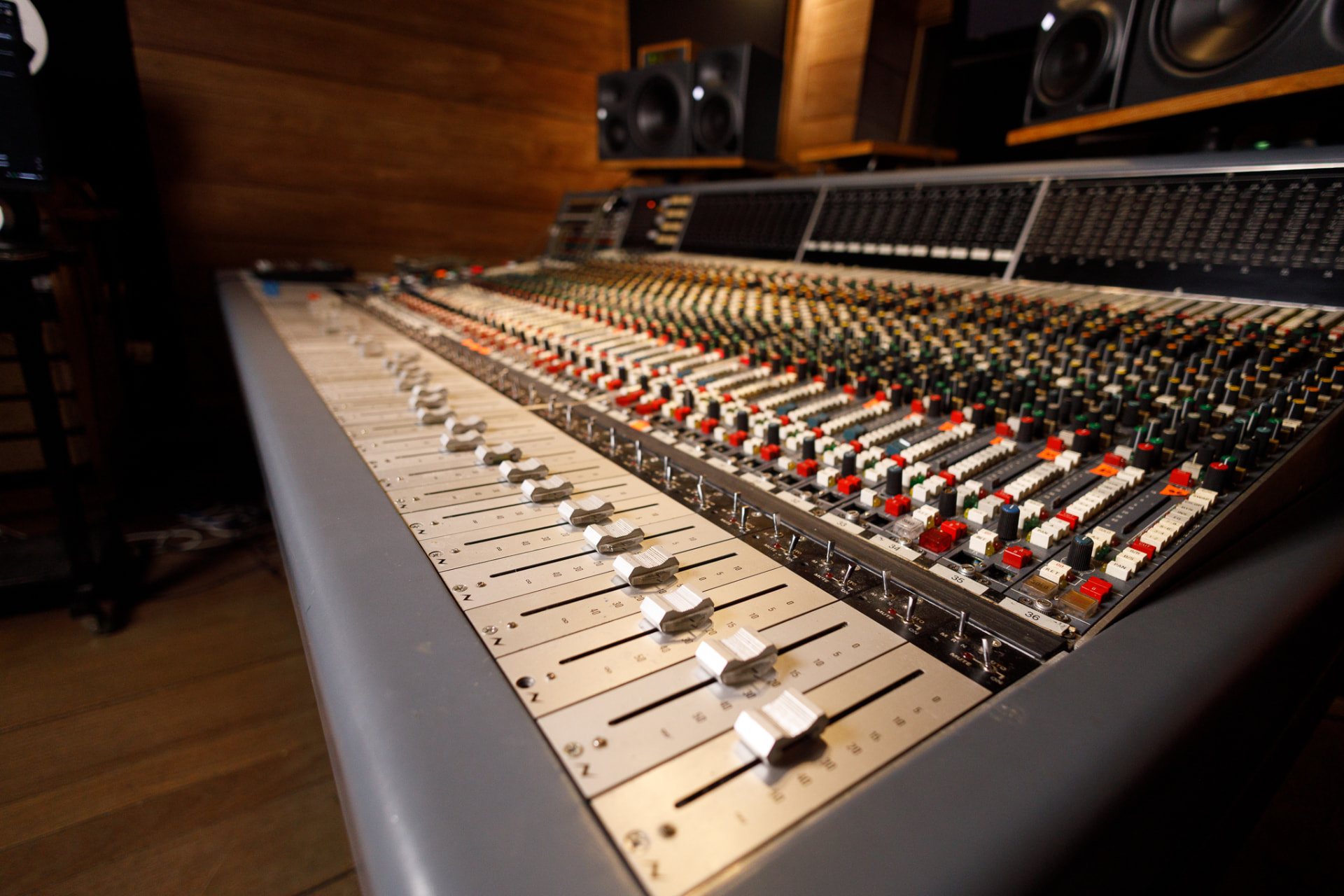Console Neve V3 em perspectiva, com faders e monitores ao fundo